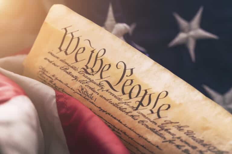 US constitution with the words "We the People" on old parchment paper on USA American Flag with warm lens flare.